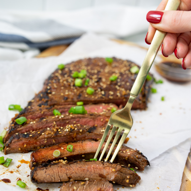 Close-up of sliced Blackstone griddle flank steak with a caramelized crust and juicy pink center on a cutting board.