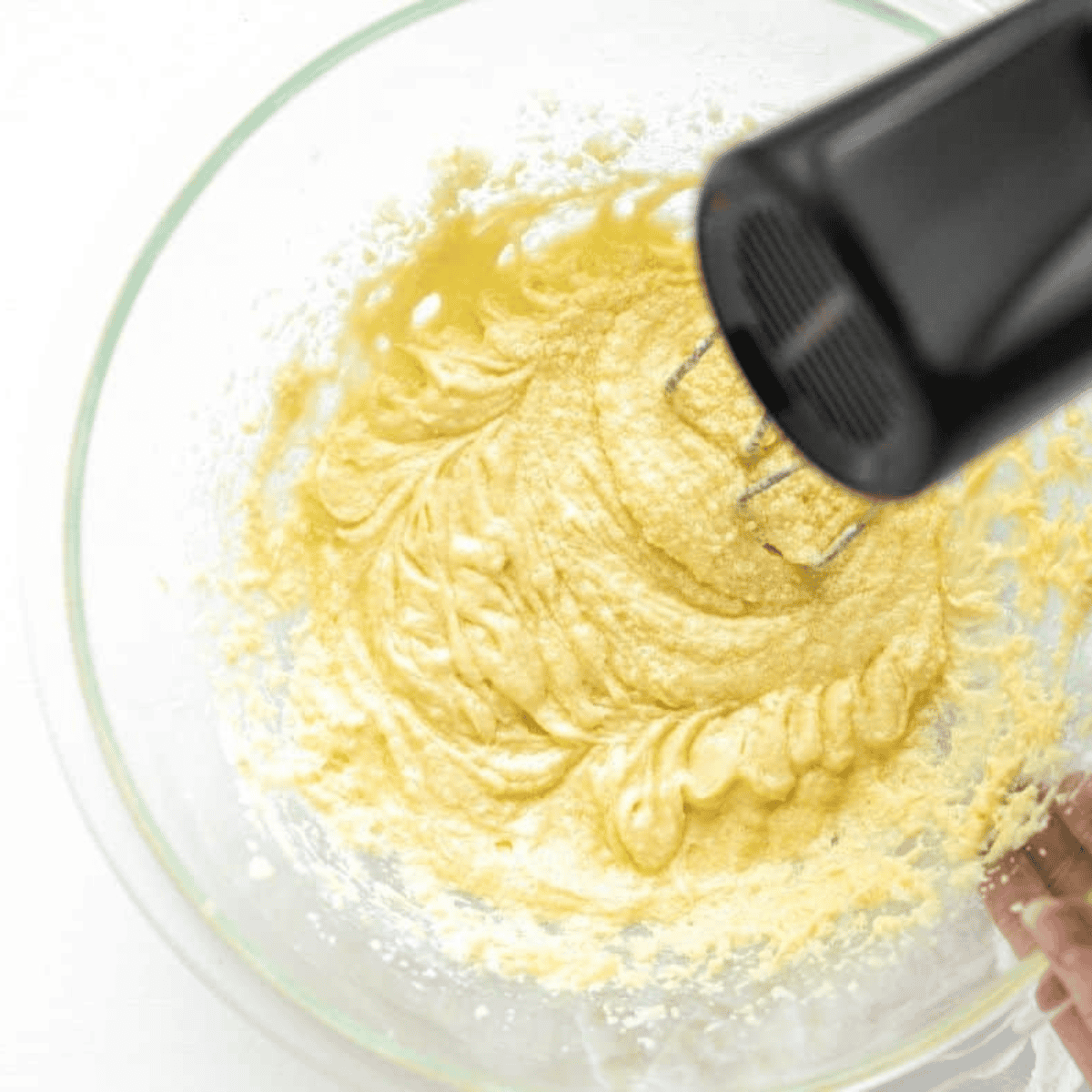Creaming softened butter and sugar, then mixing in egg and almond extract until smooth.