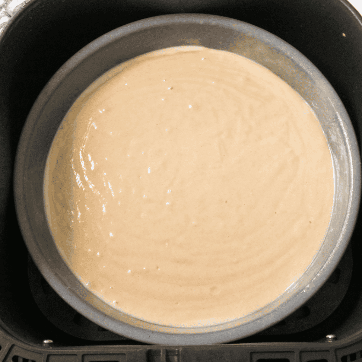 Preheating air fryer, greasing a cake pan, and pouring almond cake batter into the pan ready for baking.