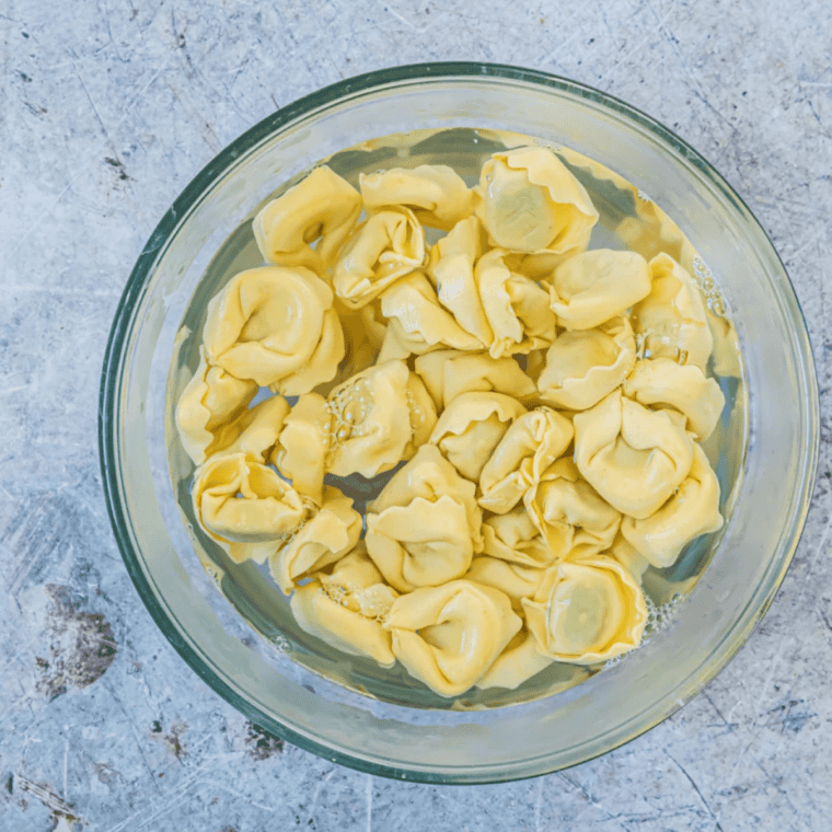 Cheese tortellini soaking in a bowl of boiling water to soften before air frying