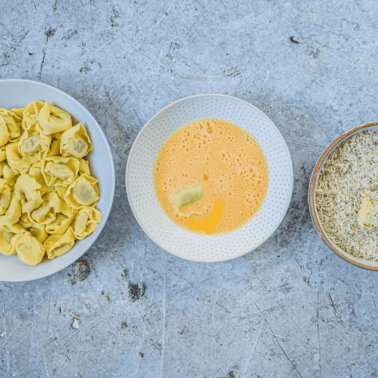 Two shallow bowls set up for breading tortellini &mdash; beaten eggs and seasoned panko mixture