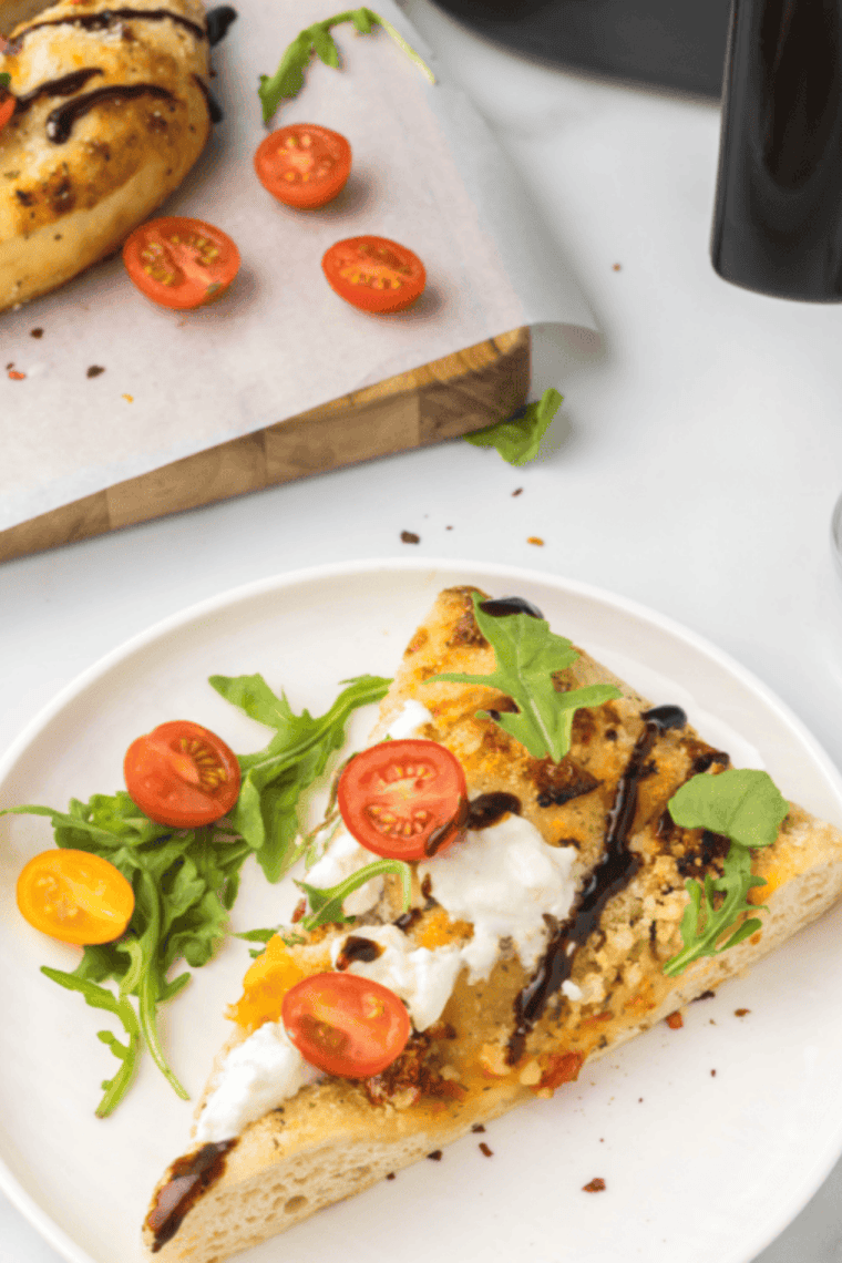 Air fryer focaccia topped with melted burrata, fresh arugula, and cherry tomatoes on a golden, crispy crust