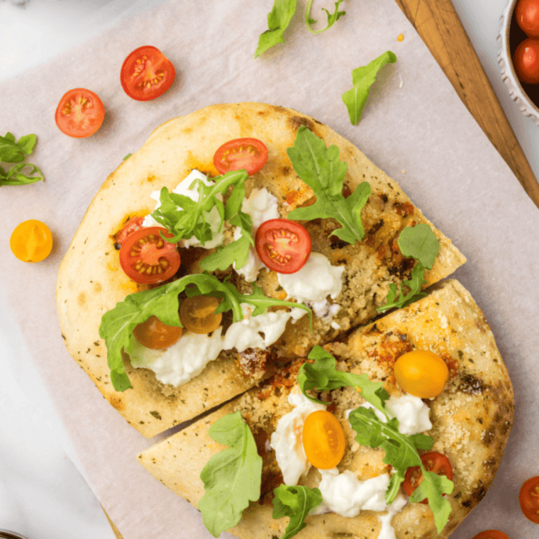 Air fryer focaccia topped with burrata cheese, arugula, and cherry tomatoes on a crispy crust