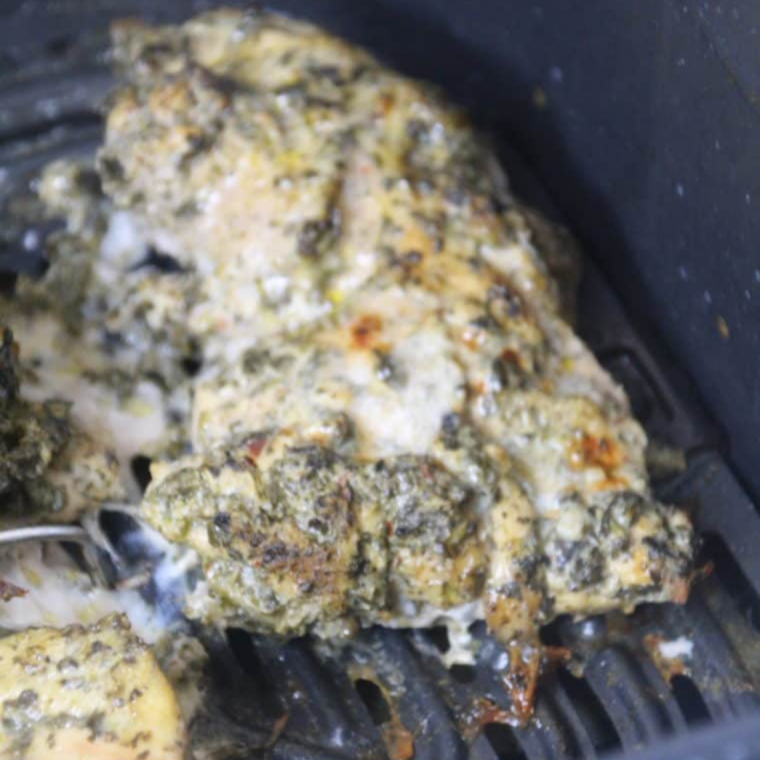 Partially cooked herbed chicken thighs flipped over in the air fryer basket halfway through cooking