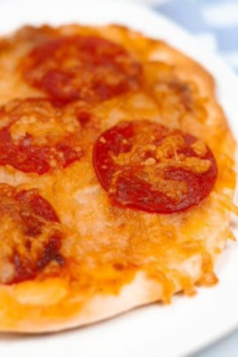 Crispy air fryer pepperoni naan pizza sliced into 4 wedges on a wooden cutting board, topped with curled cup-and-char pepperoni, melted mozzarella, and torn fresh basil leaves