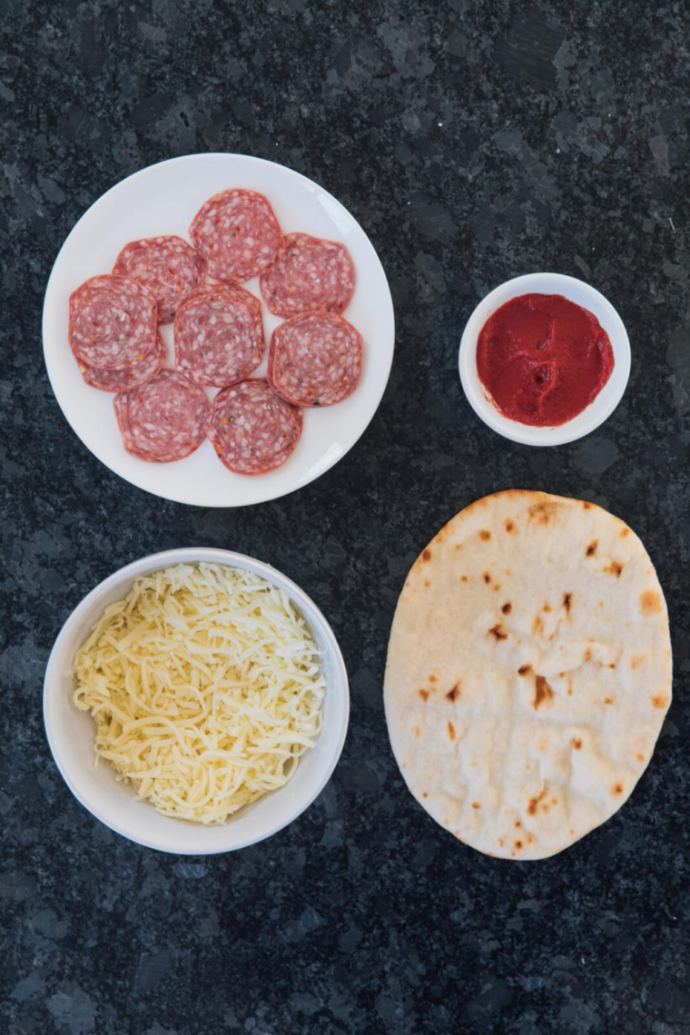 Ingredients flat lay
Air fryer pepperoni naan pizza ingredients on white marble &mdash; Stonefire naan bread, jarred pizza sauce, shredded mozzarella, pepperoni slices, Italian seasoning, and fresh basil