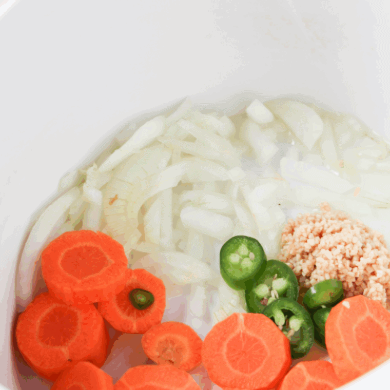 Add olive oil, onion, bell peppers, carrots, and garlic to the crock pot, cooking until the onion turns translucent.