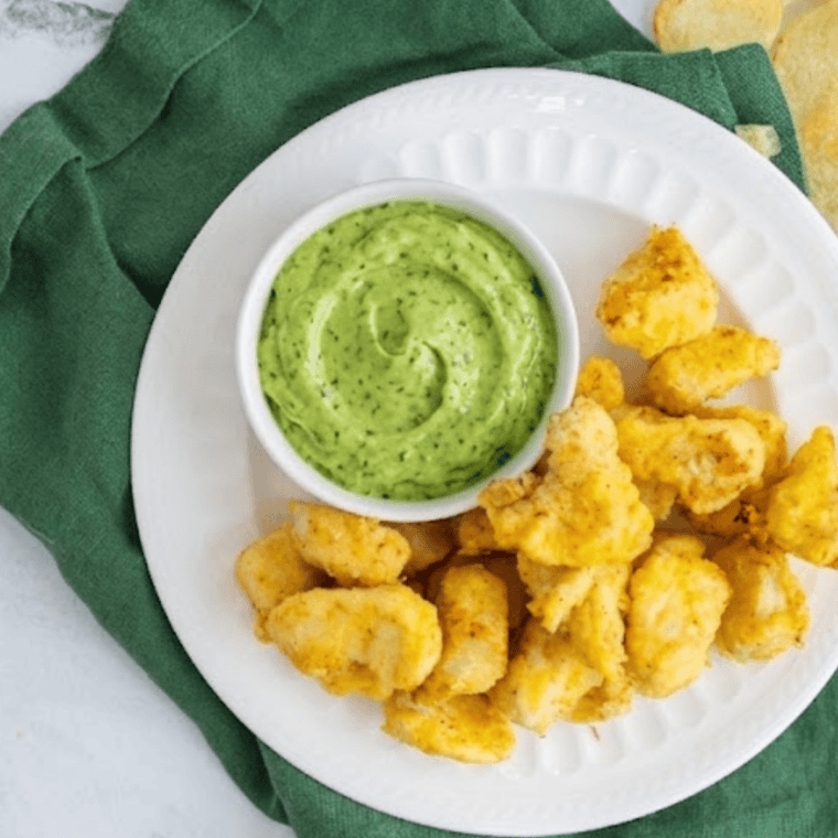 creamy avocado lime ranch dressing in bowl with fresh herbs and lime wedges
