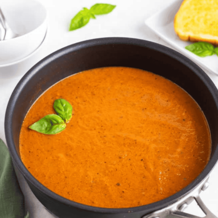 Air fryer tomato soup in a white bowl, garnished with fresh basil and a drizzle of cream