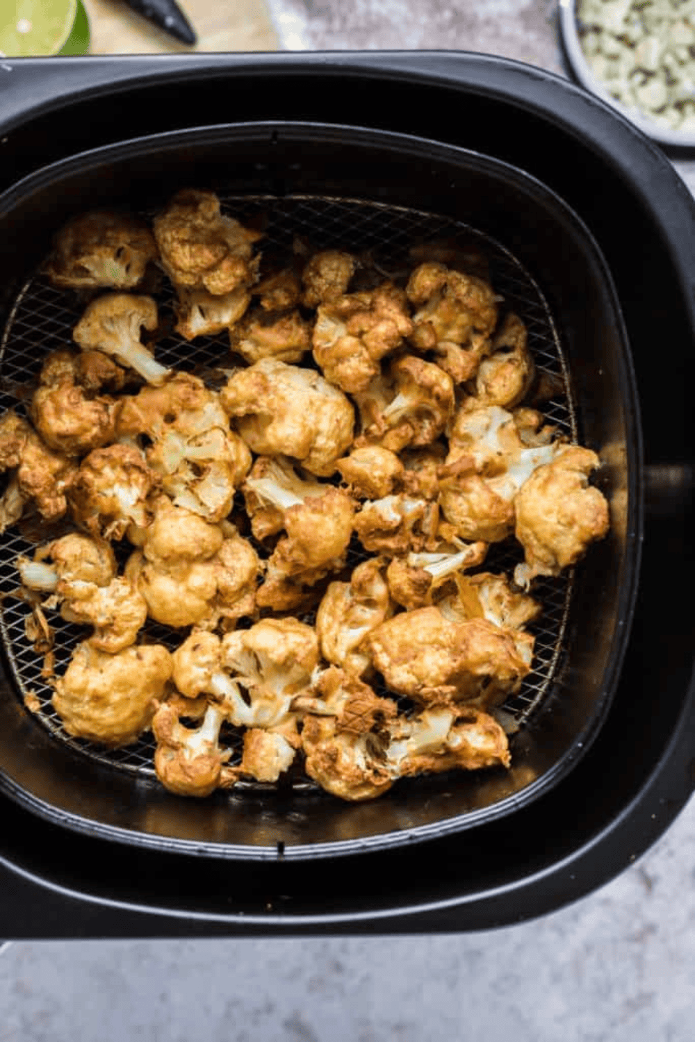 Cauliflower florets in air fryer basket, golden brown and crisp after cooking