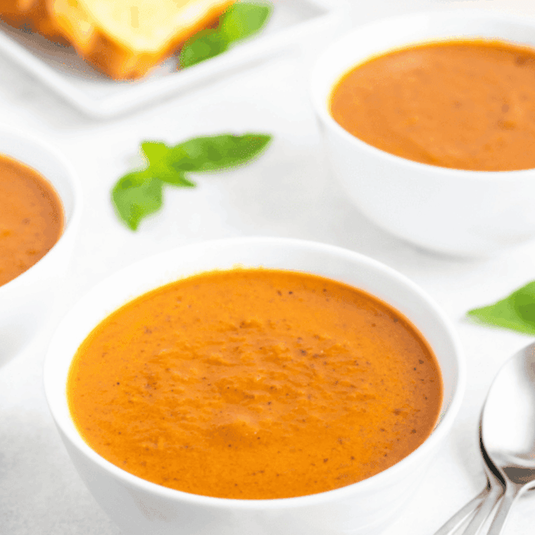 Creamy tomato soup in a bowl with fresh basil, made using the air fryer.