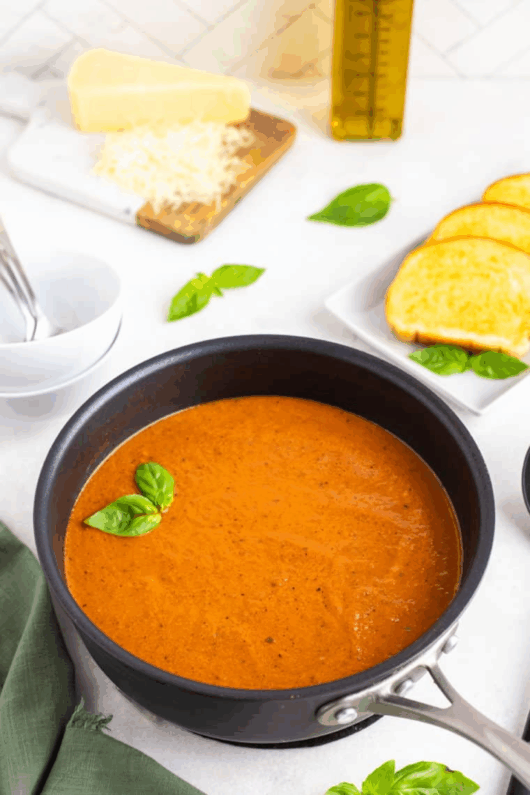 A bowl of creamy tomato soup made in the air fryer, garnished with herbs and served with a side of grilled cheese.