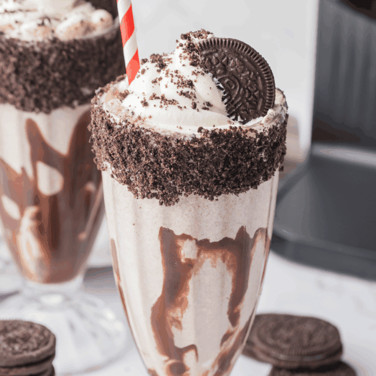 A tall glass filled with a thick Oreo milkshake made in a Ninja Creami, topped with whipped cream and crushed chocolate sandwich cookies.