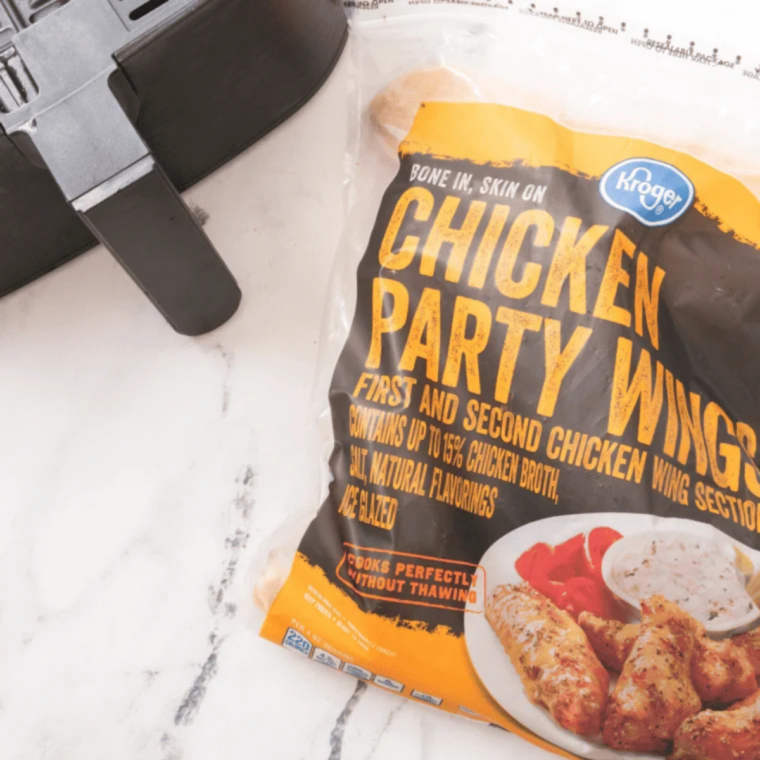 Frozen chicken wings, kosher salt, black pepper, garlic powder, smoked paprika, and buffalo sauce on a marble counter