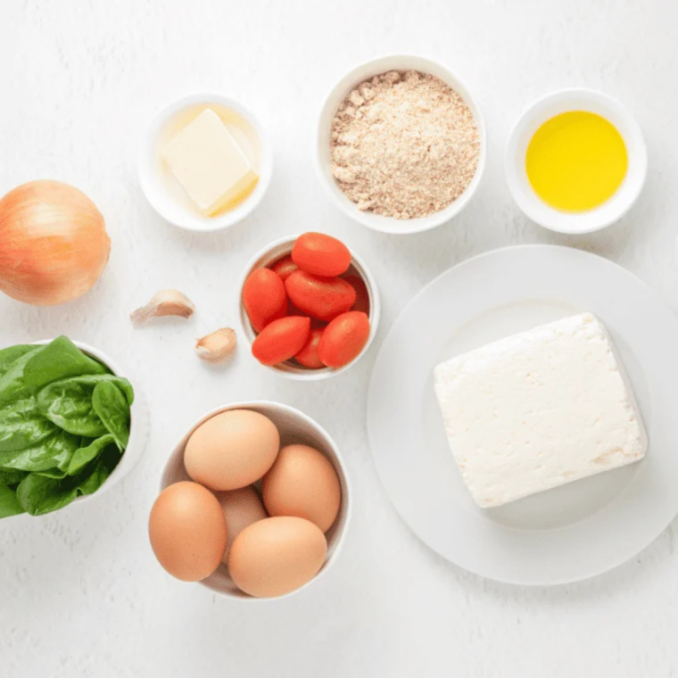 Ingredients for gluten-free quiche: almond flour, eggs, cream, spinach, cherry tomatoes, feta, cheddar, onion, and garlic