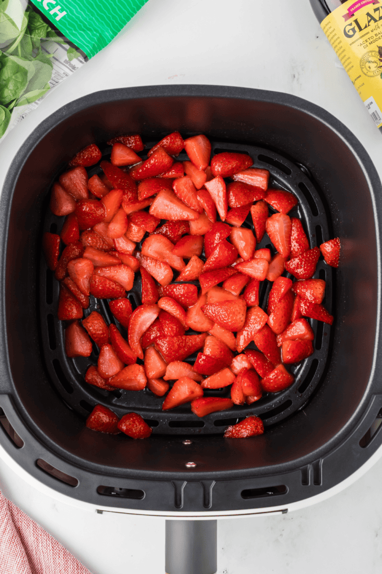 Sugared strawberry slices arranged in a single layer in the air fryer basket on perforated parchment