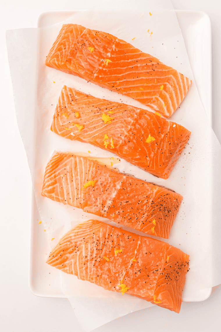 Salmon fillets being coated with honey-orange glaze in a shallow dish before marinating.