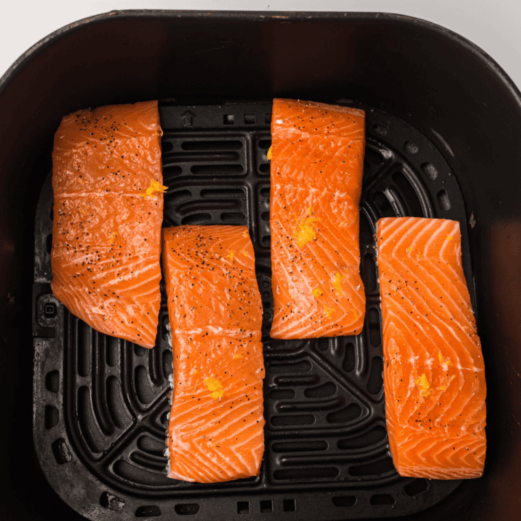 Marinated salmon fillets arranged in an air fryer basket, cooking to golden, flaky perfection.