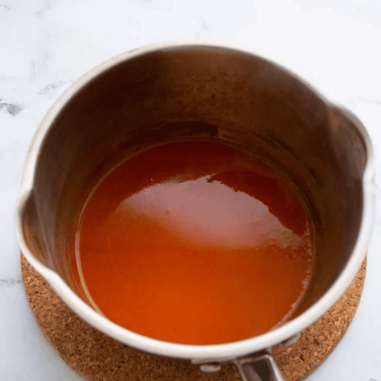 Saucepan on the stove with peach preserves, whiskey, ketchup, spices, and other ingredients being stirred together for whiskey peach BBQ sauce.