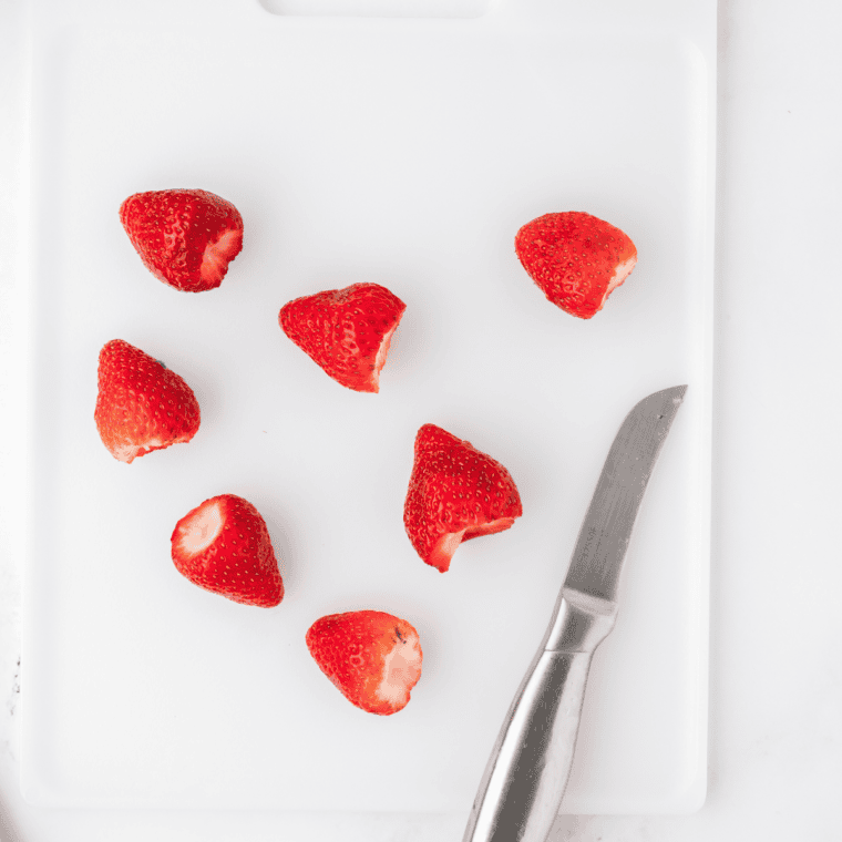 Sliced fresh strawberries on a cutting board, hulled and cut into quarter-inch pieces for air fryer strawberry candy