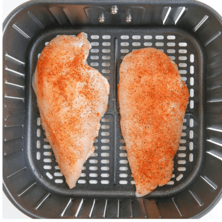 Thin chicken breast cooking in the air fryer, flipped halfway to brown both sides