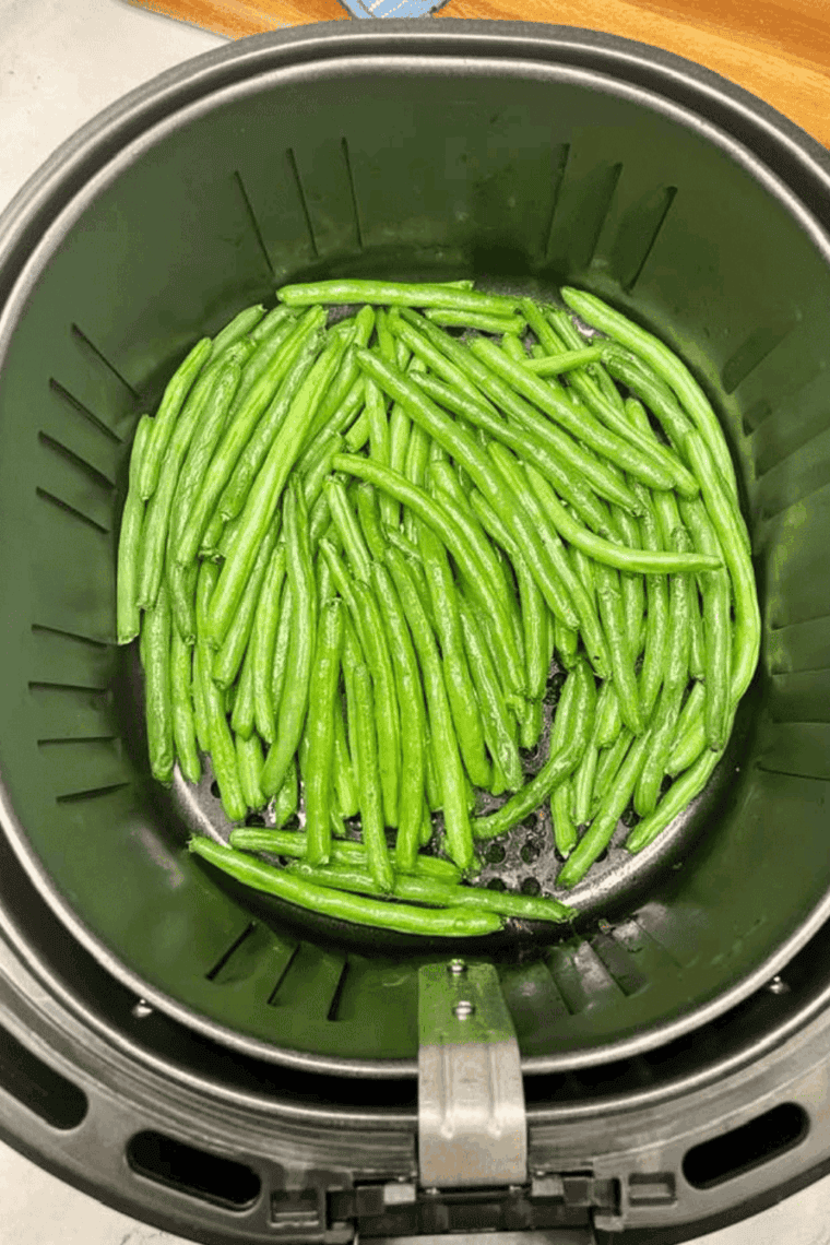 Golden brown air-fried green beans coated in rich garlic butter sauce, served in air fryer basket.