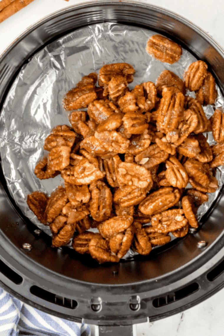 Pecans arranged in a single layer in the air fryer basket.