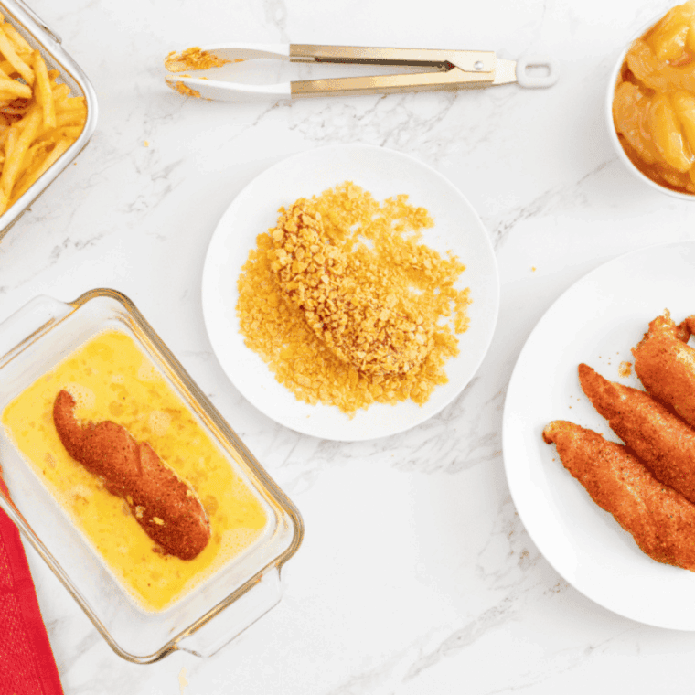 Dipping breaded chicken tenders into egg wash and coating with crushed cornflakes for extra crunch.