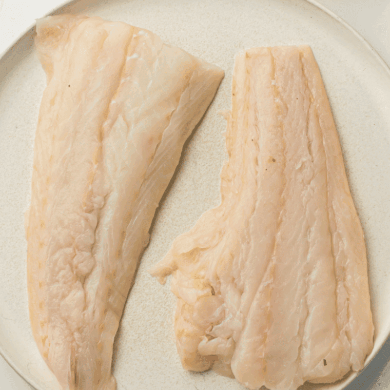 Raw cod fillets being patted dry with paper towels before cooking