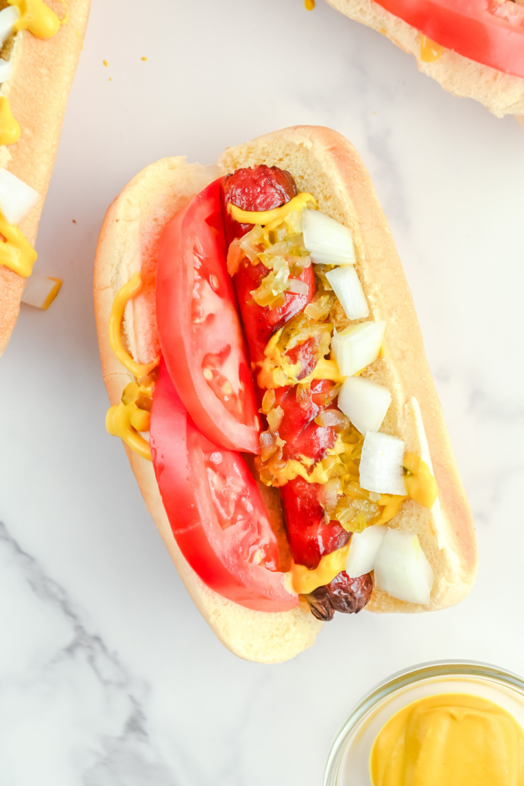 Frozen hot dogs cooking in an air fryer basket, turning hot and lightly crisp on the outside with juicy centers, ready to serve in buns.