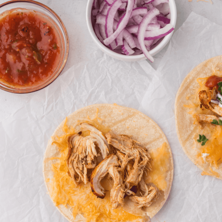 Spooning crockpot shredded chicken into a warm flour tortilla.