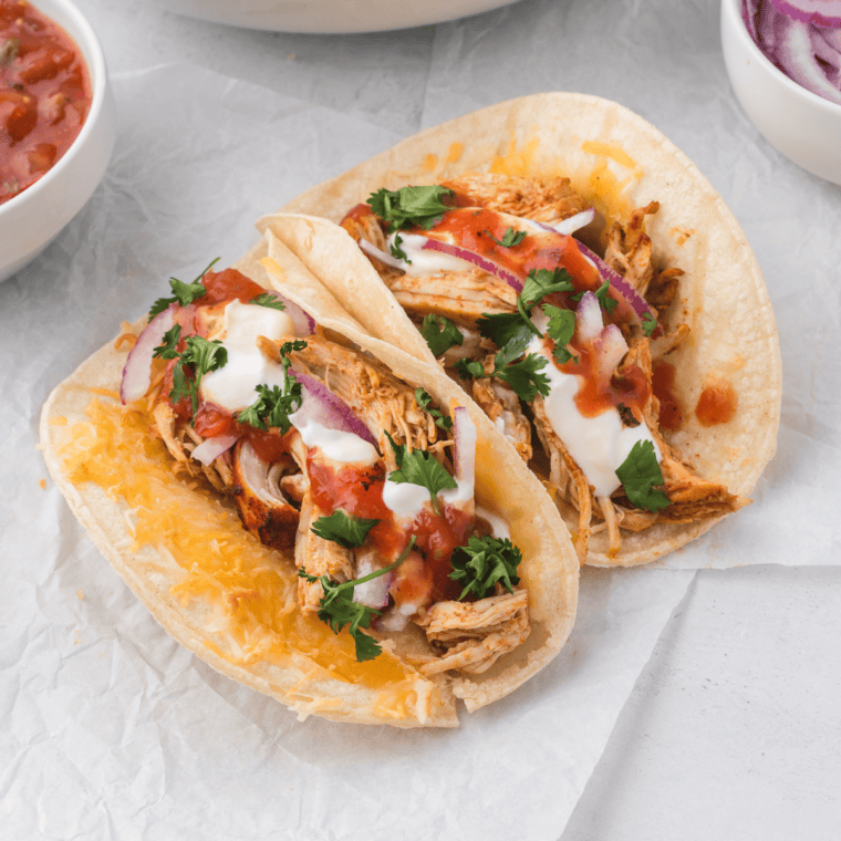 "Crockpot shredded chicken tacos topped with cheese, lettuce, and cilantro"