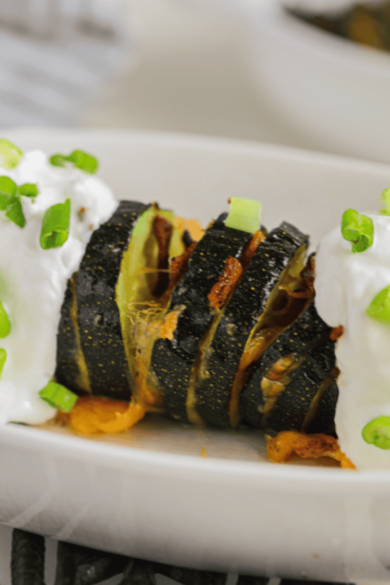 Golden-brown Hasselback zucchini in an air fryer, sliced with melted cheese and fresh herbs.