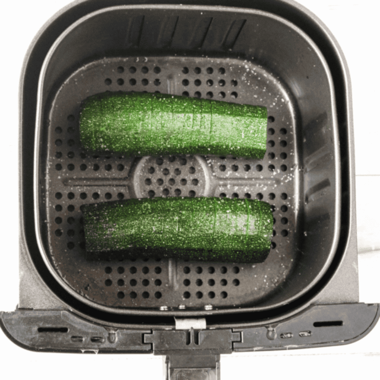 Seasoned Hasselback zucchini arranged in an air fryer basket, cooking until tender with golden, melted cheese.