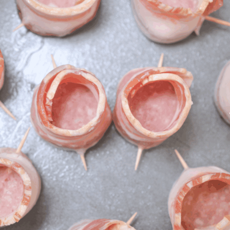 Wrapping sausage round with bacon strip and securing with a toothpick to form a cup shape.