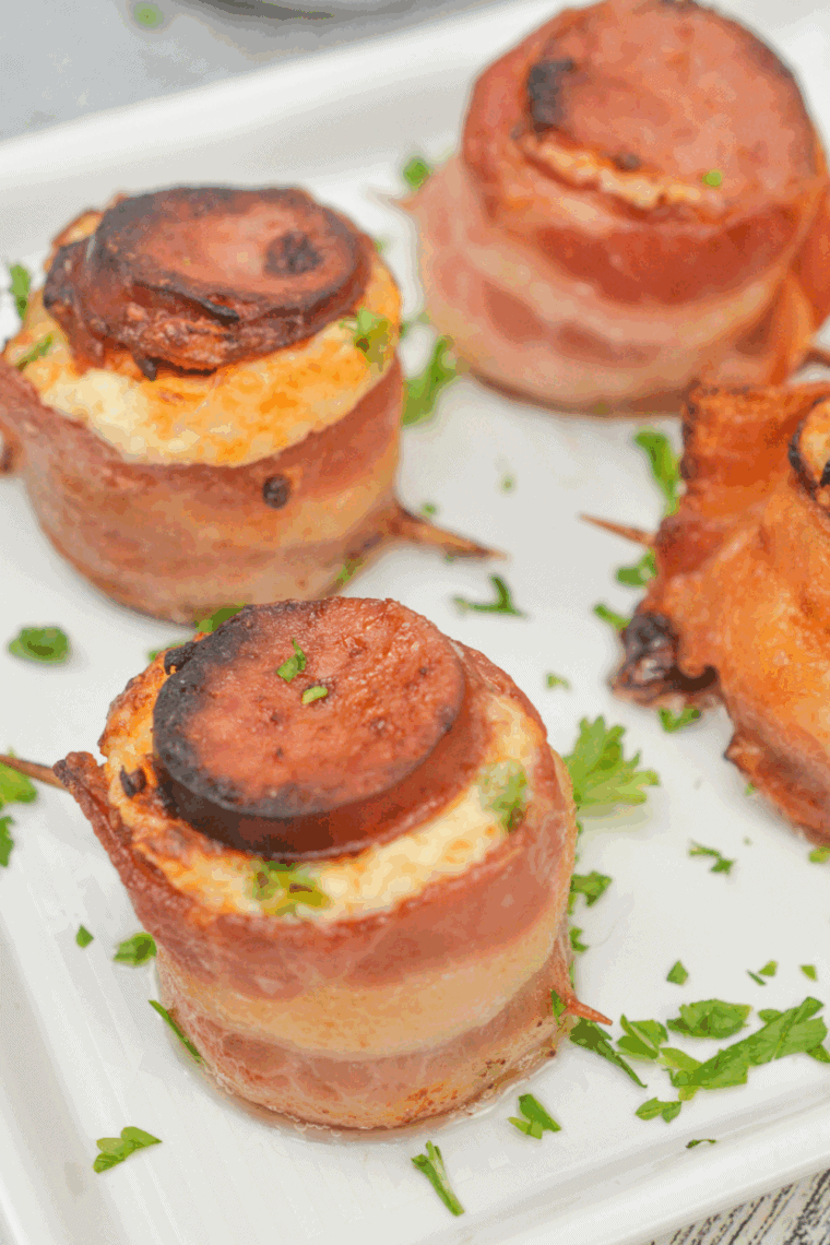 Bacon-wrapped sausage cups filled with cream cheese and cheddar, crispy and golden, served on a plate.