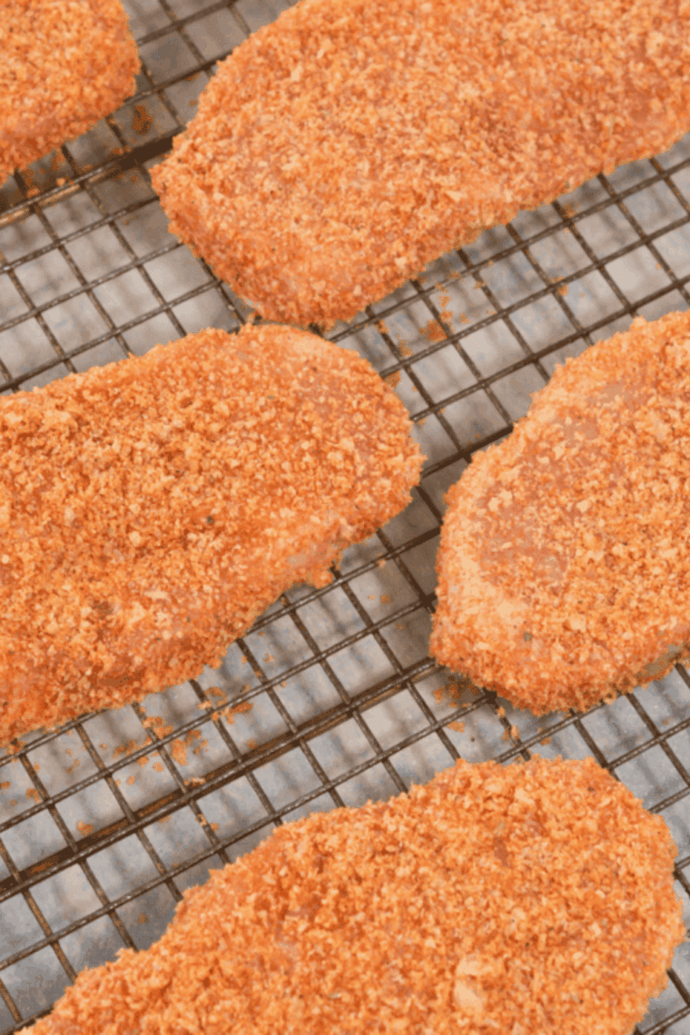 Breaded pork chops on wire rack, waiting for cooking.