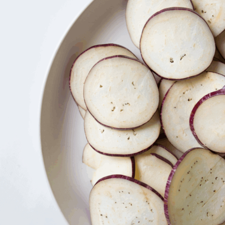 Thinly sliced eggplant rounds being cut with a mandolin slicer.