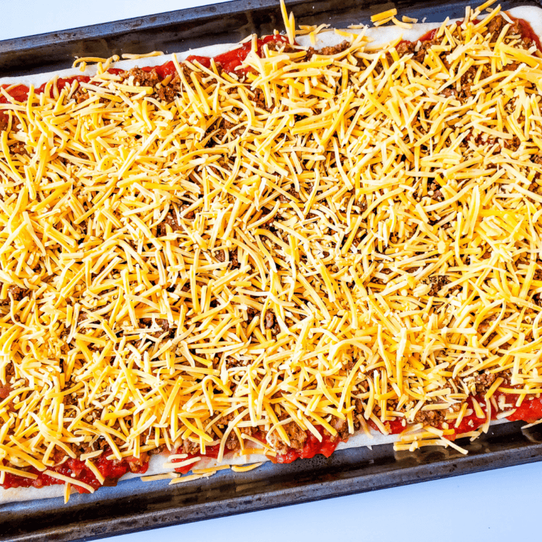 Taco pizza crust layered with salsa, seasoned beef and bean mixture, shredded cheddar, and sliced olives