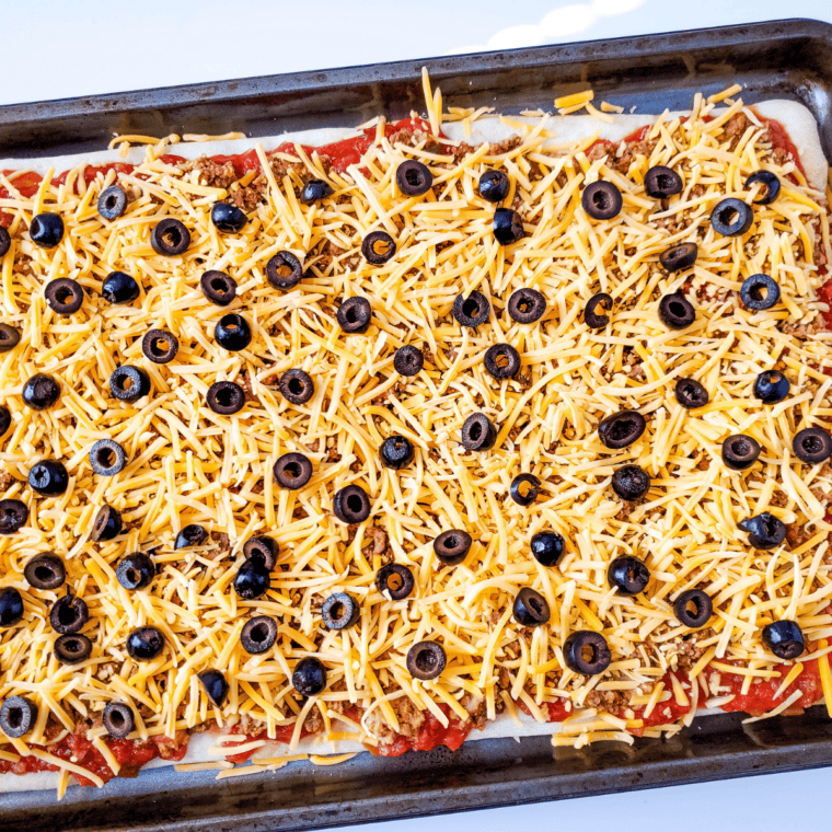 Taco pizza baking with melted, bubbly cheddar cheese and golden crust edges