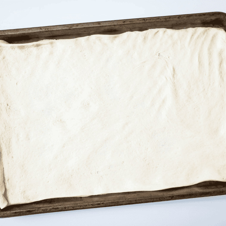 Refrigerated pizza dough pressed onto a greased baking sheet, ready to pre-bake for taco pizza