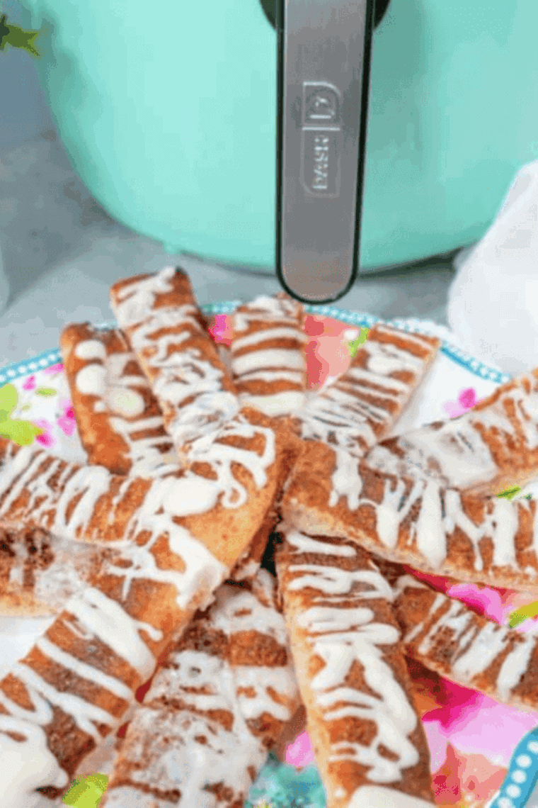 A pile of golden-brown air fryer cinnamon sticks dusted with cinnamon sugar next to a cup of white icing.