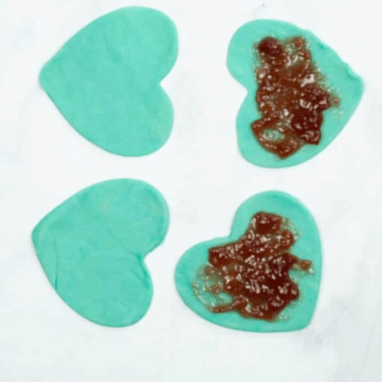 Adding a spoonful of jam to the center of a pie crust rectangle on a parchment-lined tray, leaving space around the edges for sealing.