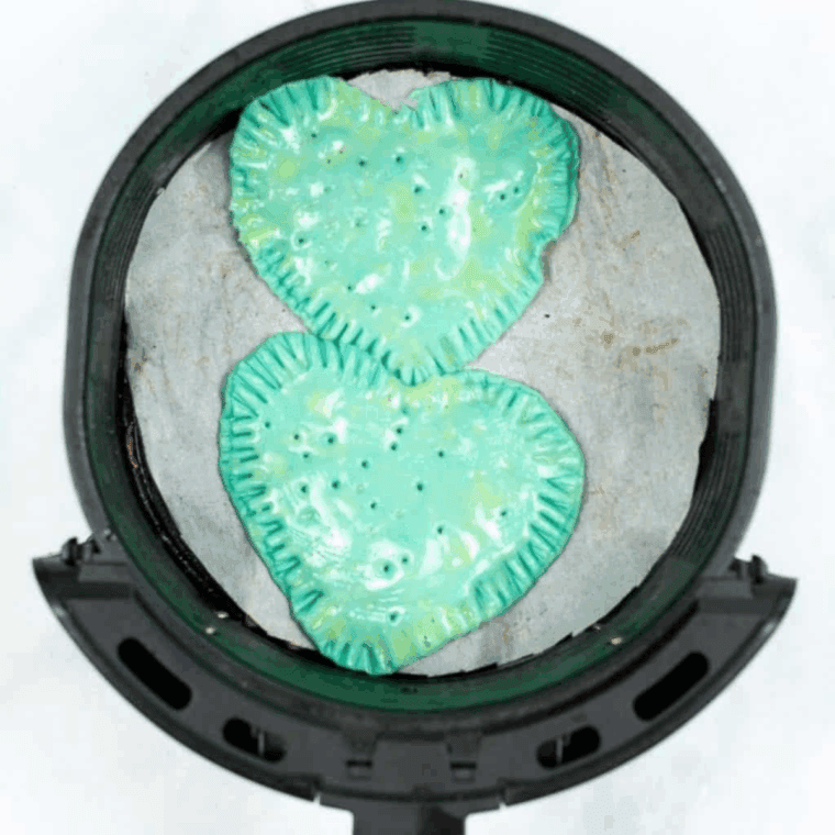 Air frying heart-shaped pop-tarts in an air fryer basket at 350°F until golden brown and crispy, with space between each for even cooking.