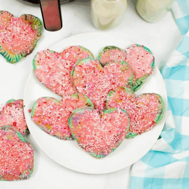 Heart-shaped Valentine’s Day pop-tarts made in the air fryer, filled with jam and topped with pink icing and sprinkles.