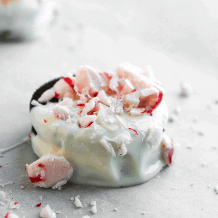 Stack of finished Peppermint White Chocolate Covered Oreos, dipped in white chocolate and topped with bright red crushed peppermint candies.