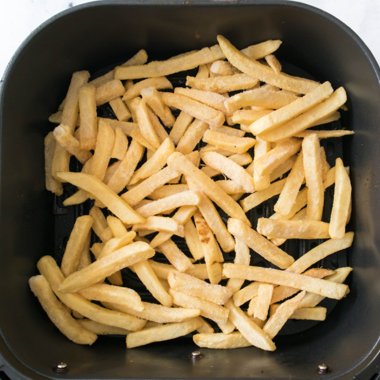Frozen French fries arranged in an air fryer basket, lightly sprayed with cooking spray, cooking to golden, crispy perfection.