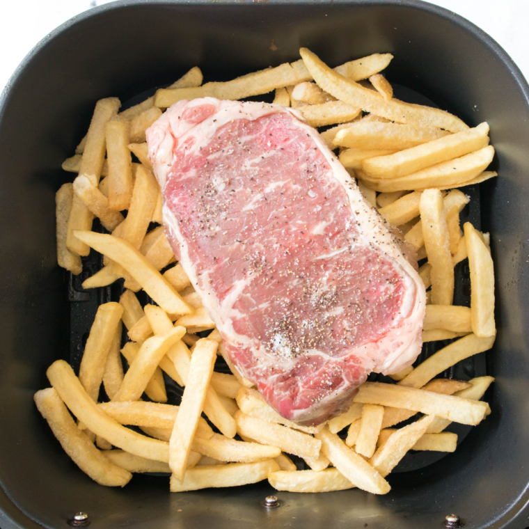 Seasoned steaks in an air fryer basket, lightly sprayed with cooking spray, cooking to desired doneness at 400°F.