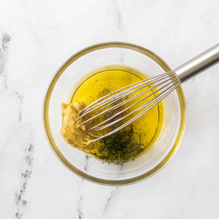 Small bowl with extra-virgin olive oil, white wine vinegar, honey Dijon mustard, and seasonings being whisked together.