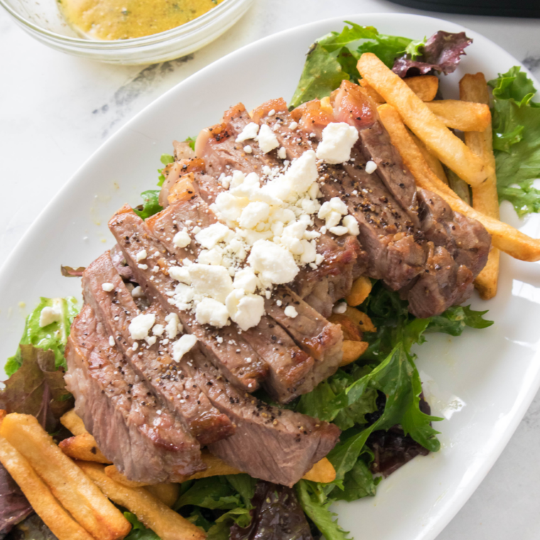 Juicy air fryer steak served with crispy golden fries on a plate, garnished with herbs.